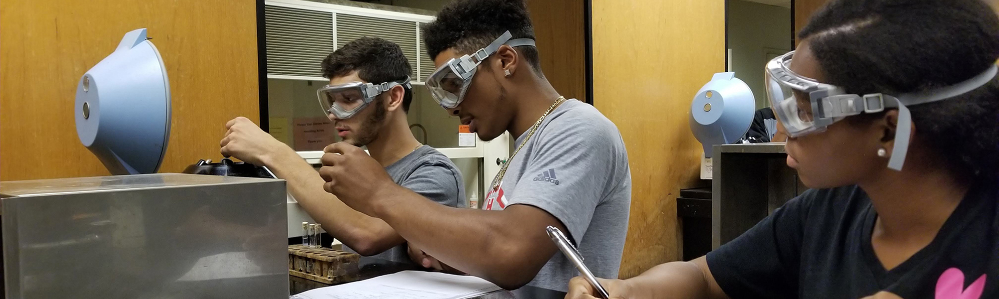 Three students with safety goggle on work in a lab with test tubes