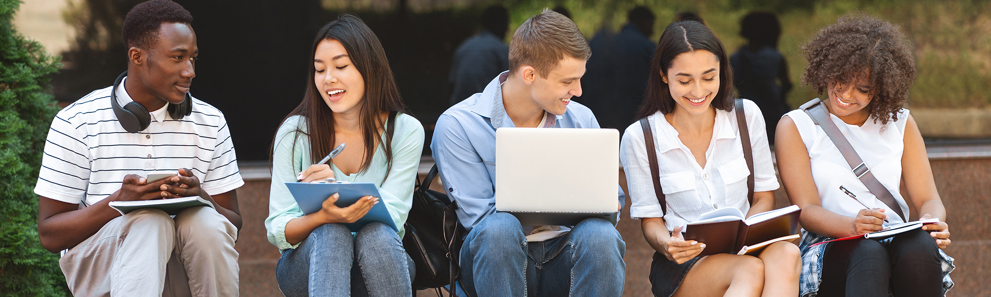 diverse college students sitting on a stone bench with laptops