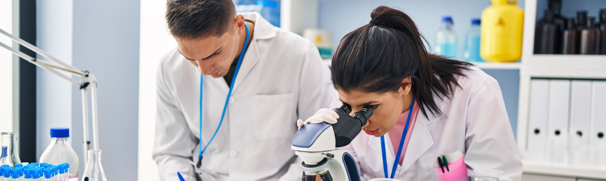 Two scientists, a man and a woman, work in lab, working with a microscope