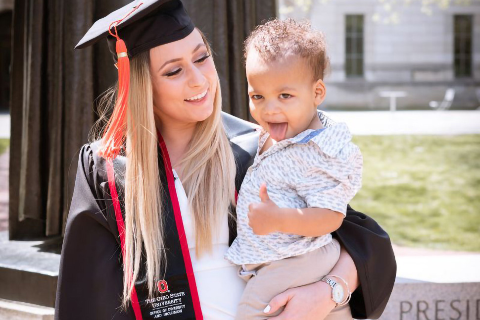 ACCESS Scholar in cap and gown, holding her child at graduation
