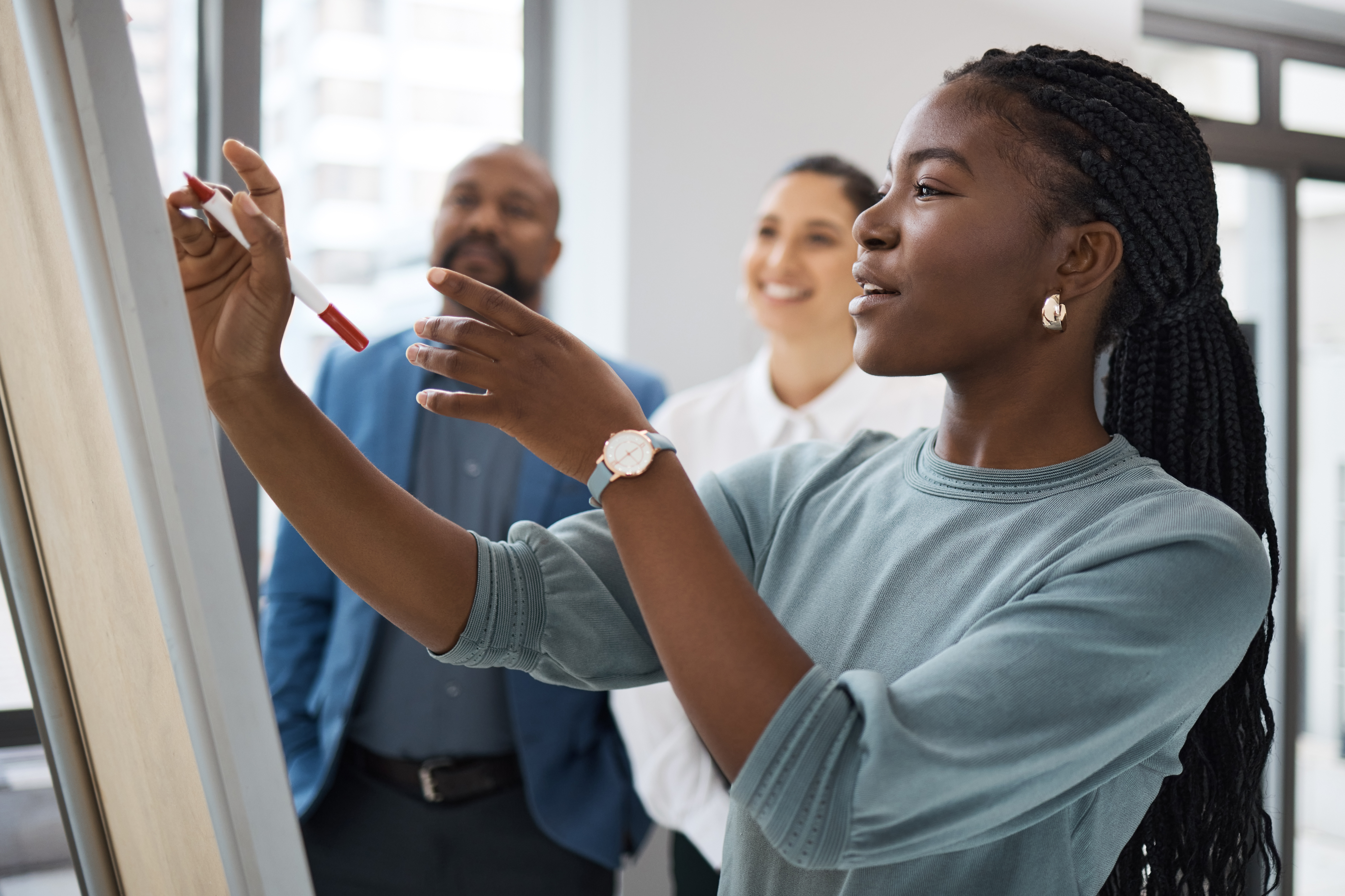 Woman writes on a whiteboard as others look on.