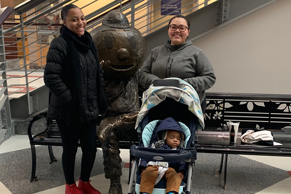 two moms with a child in a stroller stand in front of Brutus Buckeye