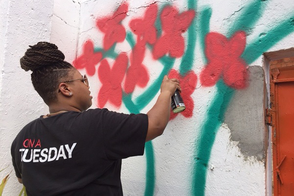 Girl in a black t-shirt spray paints bright fuscia flowers with green stems