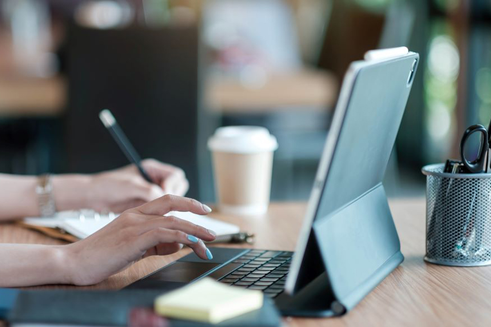 Female types onto a laptop with one hand while writing in a notebook