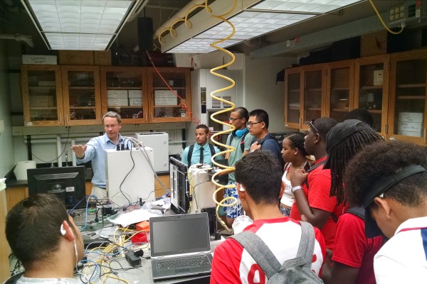 Students stand around a professsor in a mechanical engineering lab