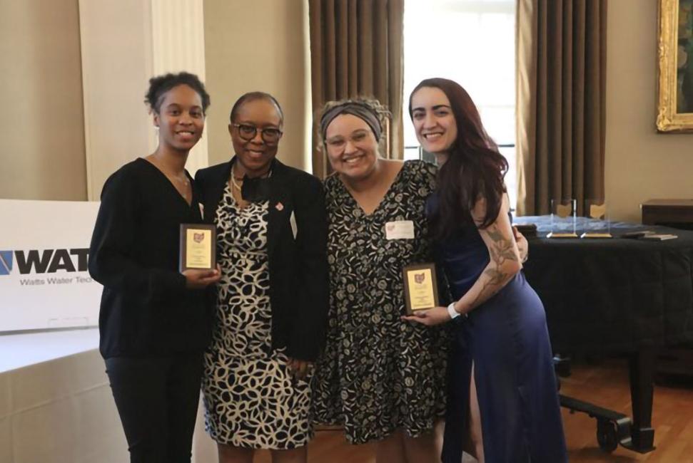 Four women stand together. The two on the end hold small awards