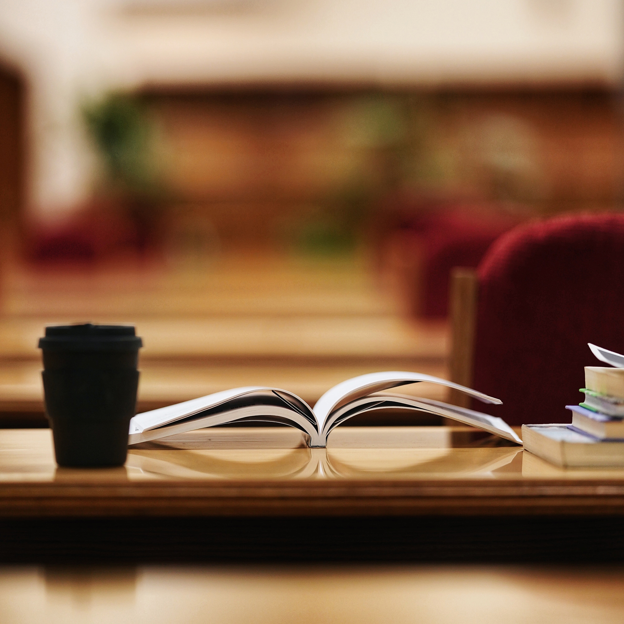 an open book on a table with a coffee cup and papers next to it