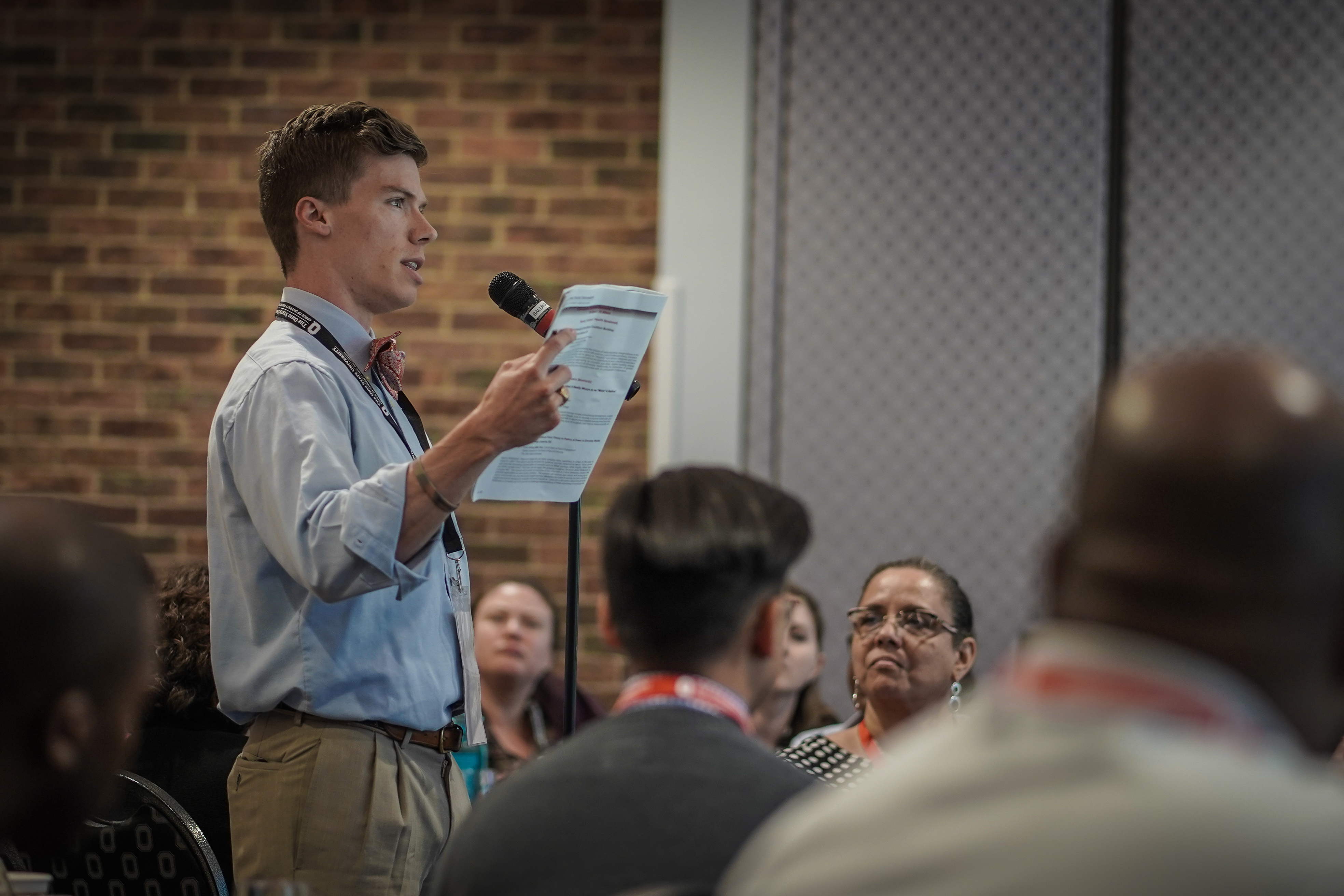 Man holding a piece of paper talking into a microphone