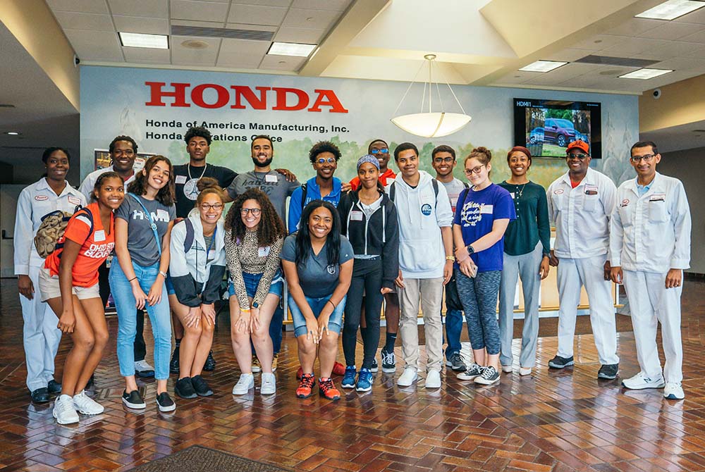 A group of students stand in front of a wall with the Honda logo