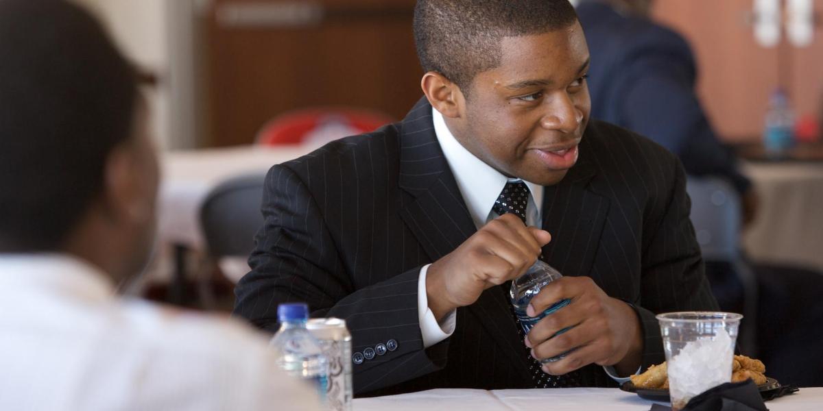 Young Black man sitting at a table in a suit with a bottle of water in his hand