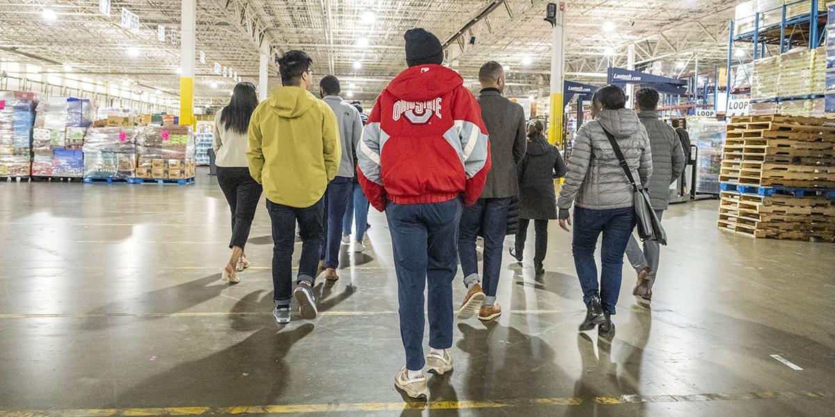 Student walk away from the camera inside the Aldi warehouse. They have jackets on.