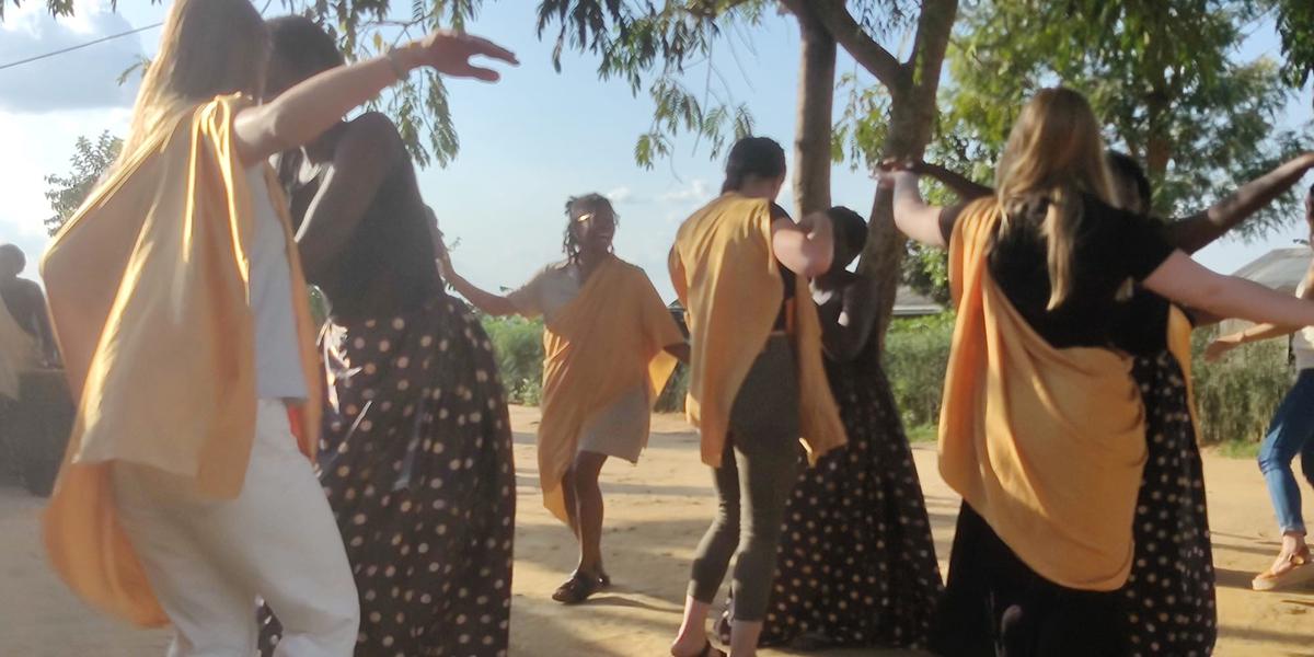 Alanna Strickland, a Black woman, dances with Rwandans while wearing yellow capes