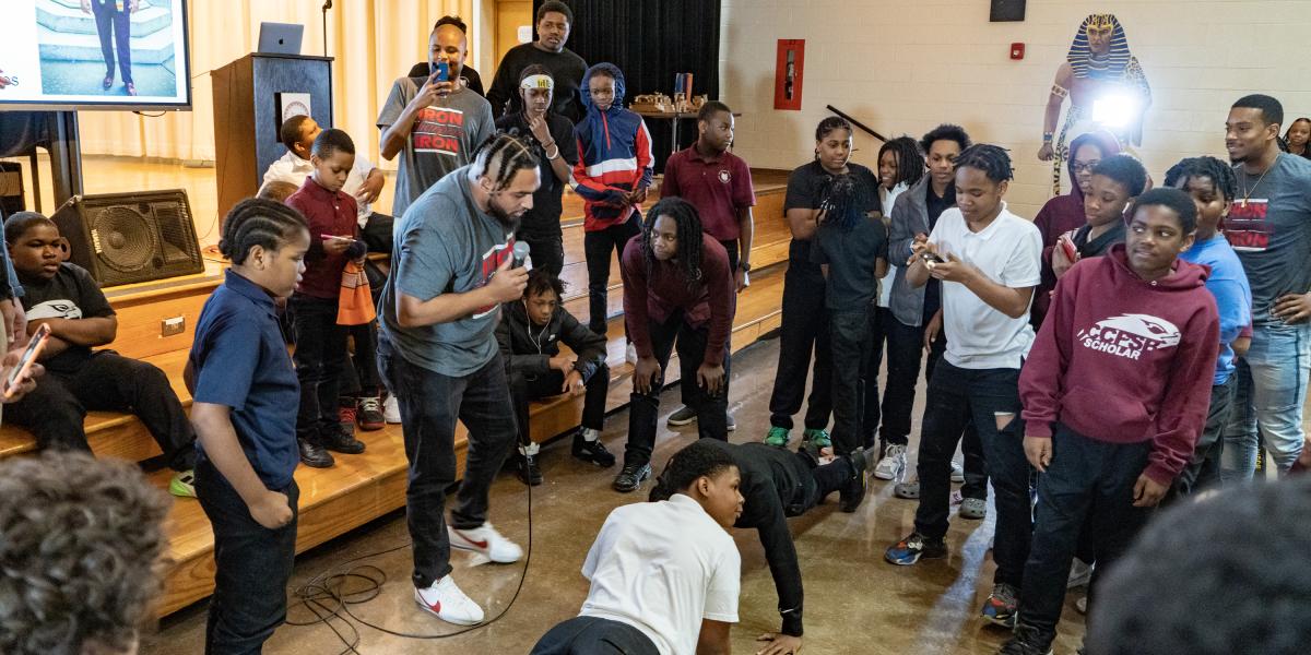 Goup of young men standing in a circle looking at two boys doing pushups