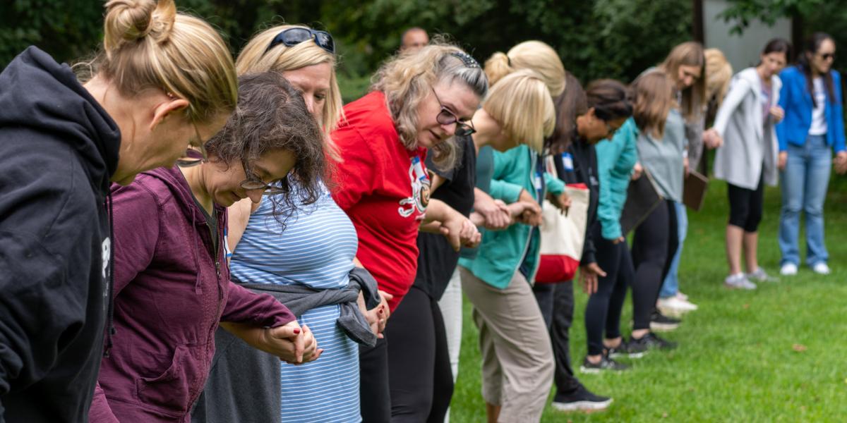 Group of women stand in line holding hands.