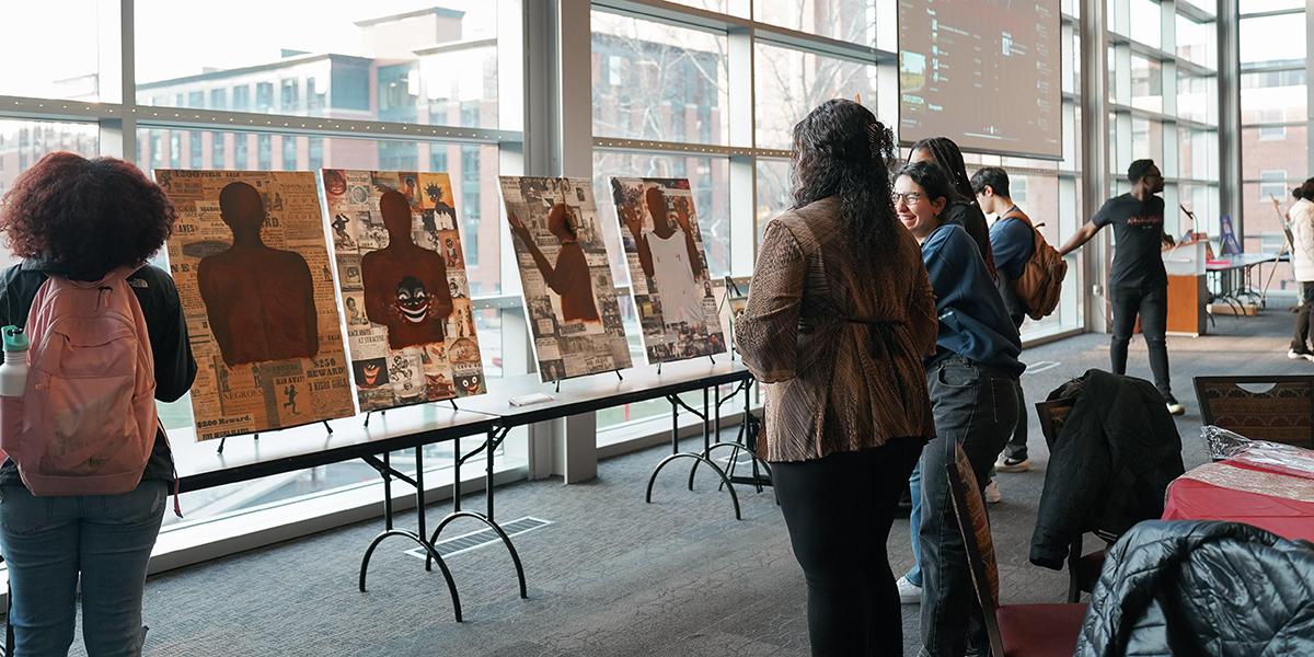 Students look at paintings of brown bodies placed in front of large windows