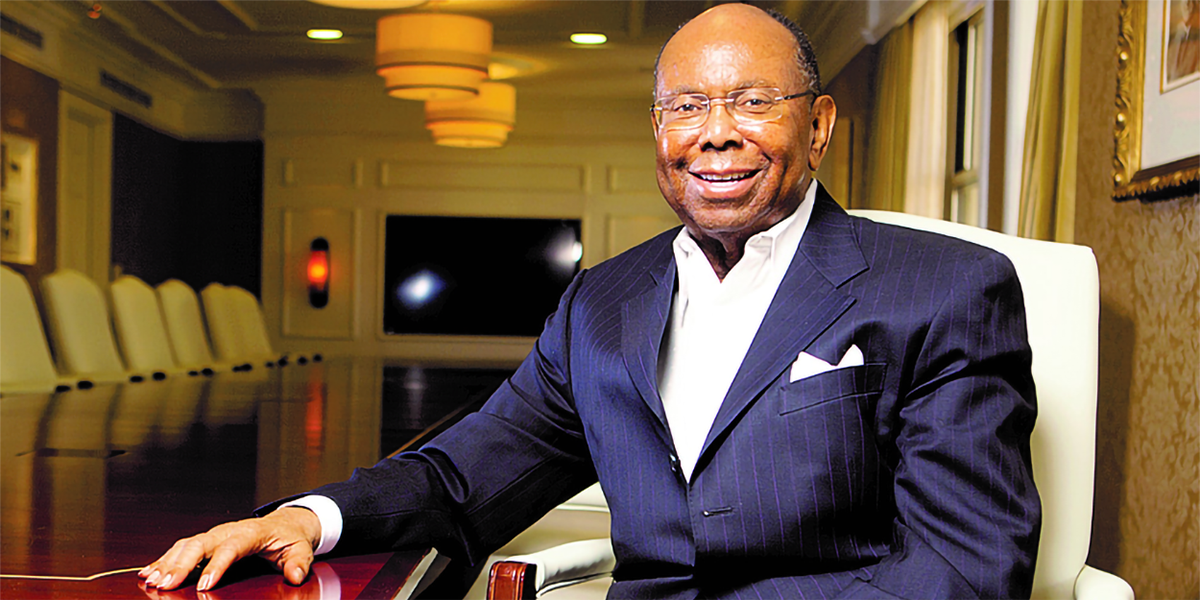 William Pickard, a Black man, sitting at a conference table in a blue pin striped suit and white shirt