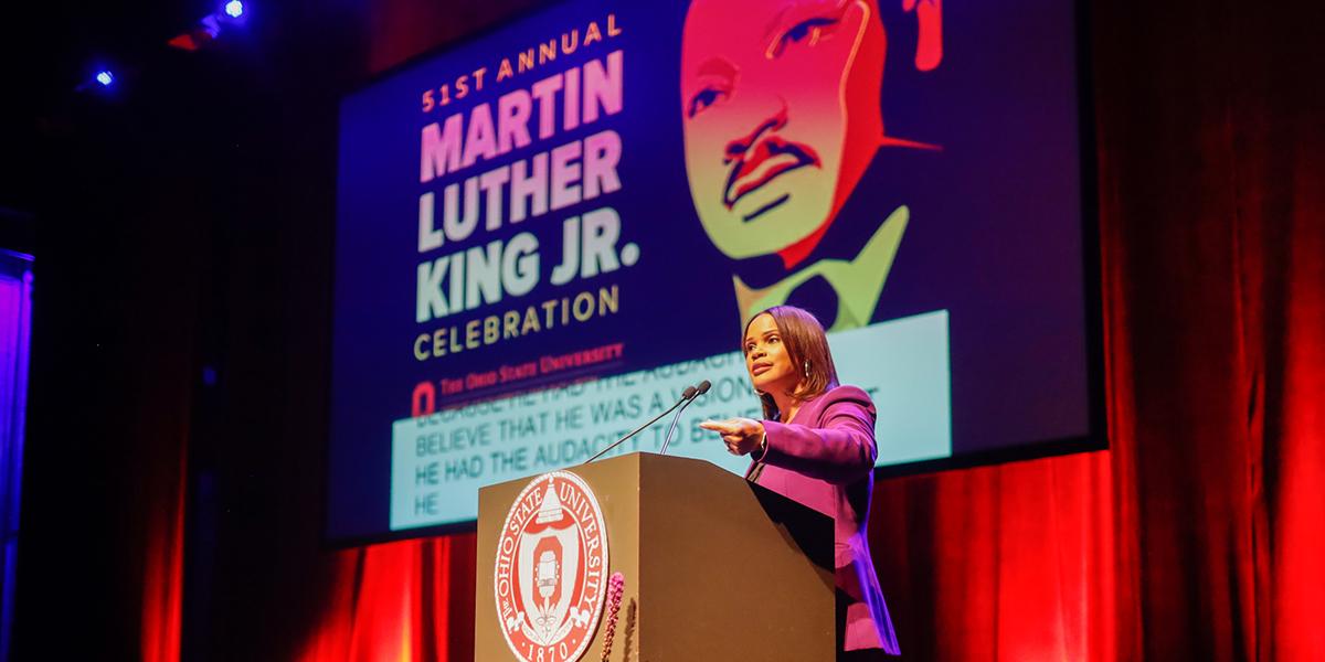 Laura Coates, a woman of color, speaks from a podium during MLK Celebration