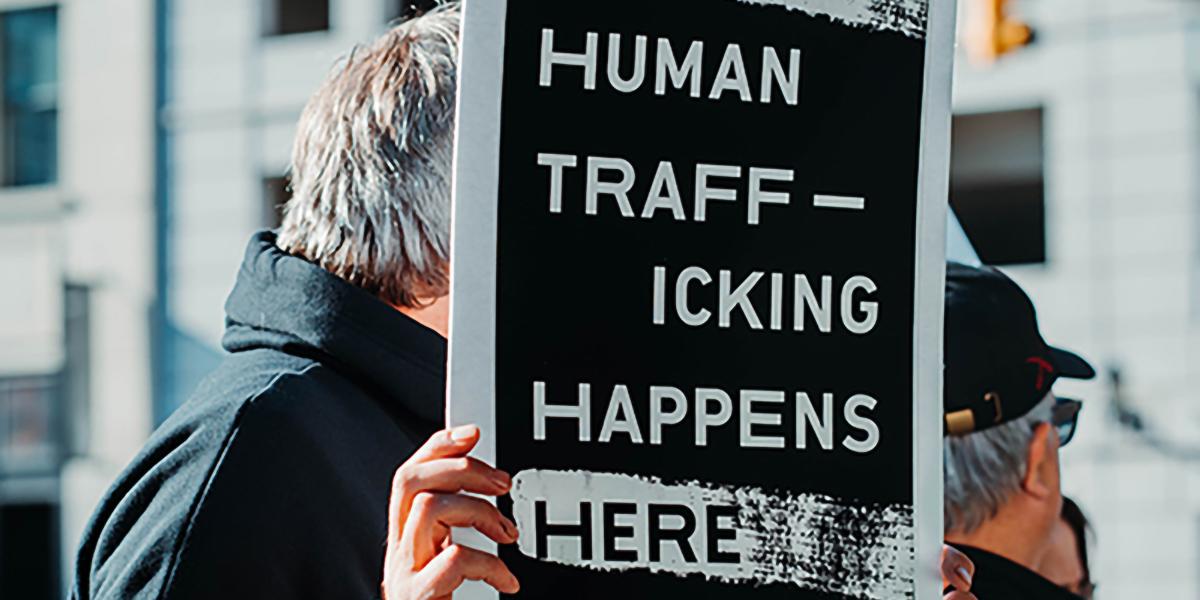 White man with grey hair holding a sign that says, "Human trafficking happens here."