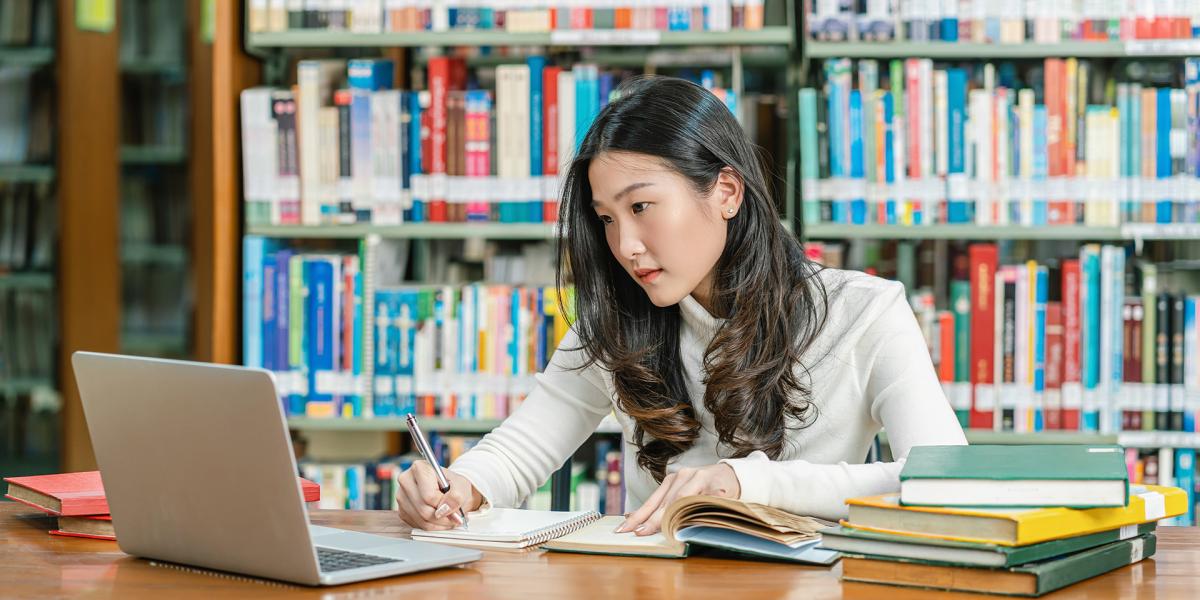 Woman college student does research at the library with open books and a laptop