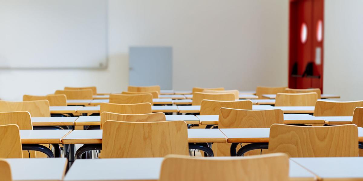 wooden desk chairs at white tables in a classroom.