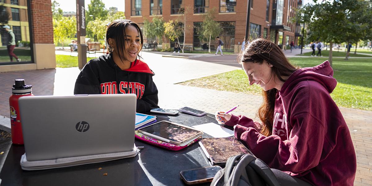 Two students at Ohio State sit outside and work together on class materials.