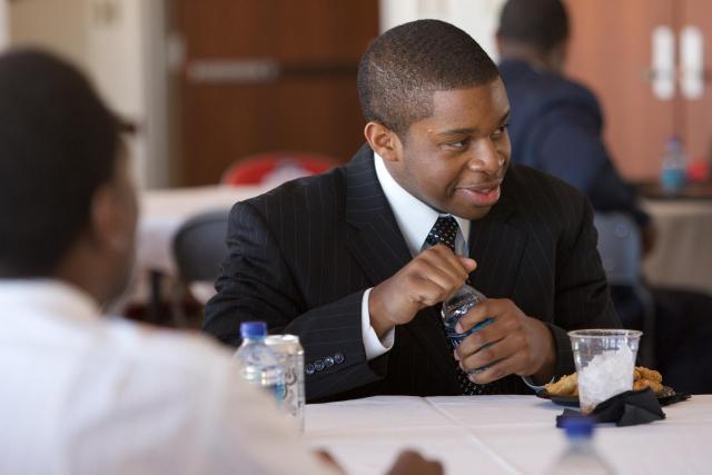 Young Black man sitting at a table in a suit with a bottle of water in his hand