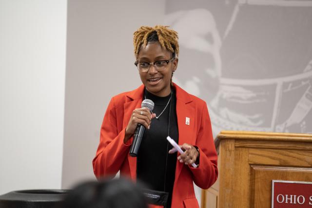 Woman in a red blazer speaking on mic