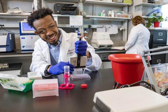 Student in purple gloves and a white lab coat works in a lab with a pipette