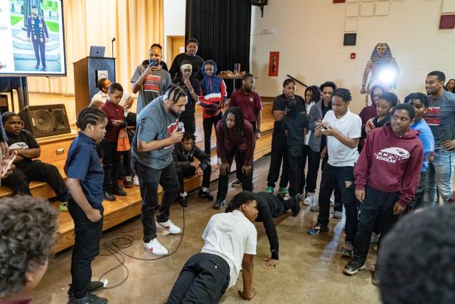 Goup of young men standing in a circle looking at two boys doing pushups