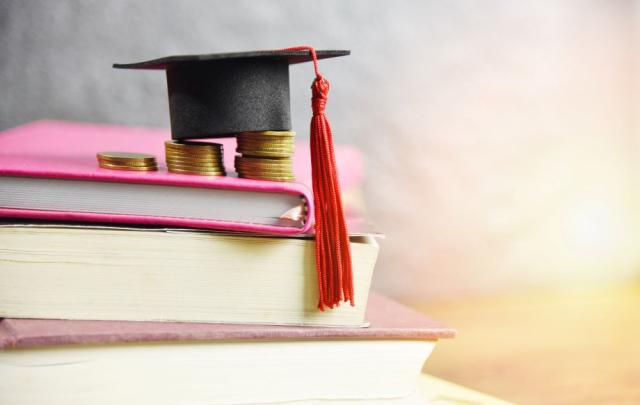 a pile of book with coins stacked on them and a gradation cap with tassel on top of that