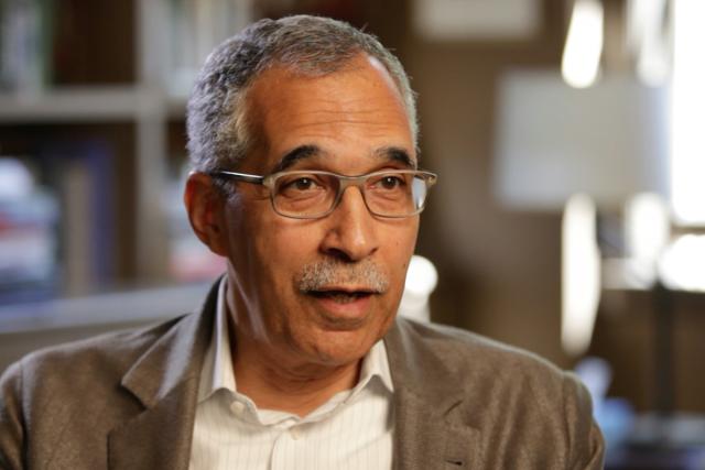 Claude M. Steele, PhD in glasses in his office wearing a tan jacket and open neck cream checked shirt