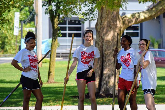 four MSP students in white Morrill Scholars t-shirts hold gardening tools in a yard