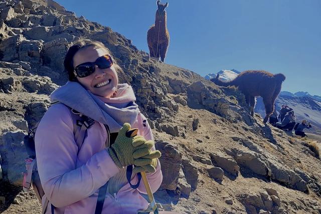 Jaquelyn Saldana sitting on a mountain in Peru with llamas behind her.