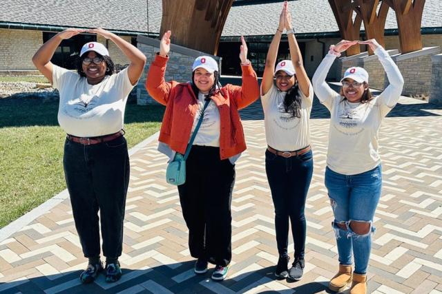 Women wearing Block O caps raise their hands in OH-IO