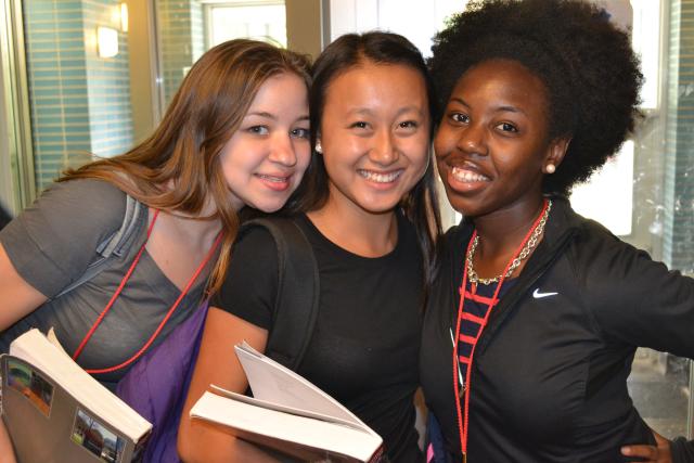 Three Young women holding textbooks and linking their arsm around each other