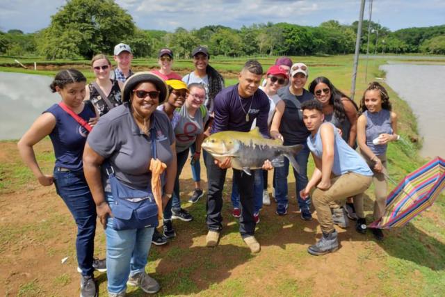 Students in Panama stand in front of a river with a large fish that they caught