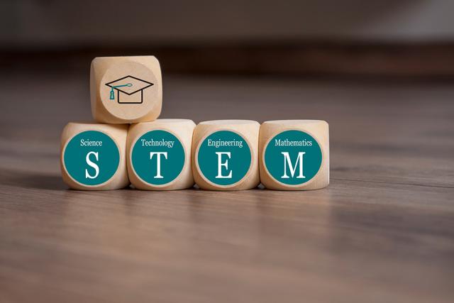 Wooden blacks that say STEM with a wooden block on top with a graduation cap