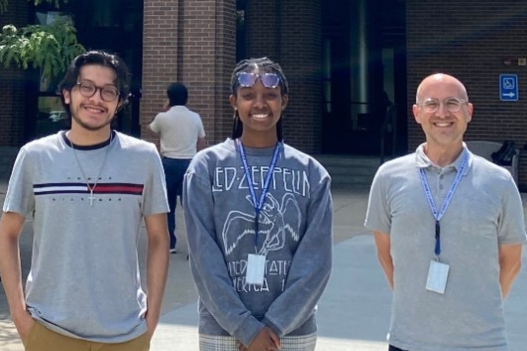 Two students and one professor stand in front of a college building