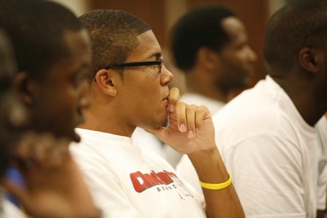 Side profile of a Black man with his hand holding his head, wearing glasses