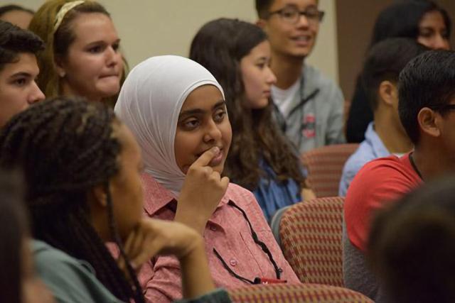 woman in a headscarf listens to speaker along with other male and female students