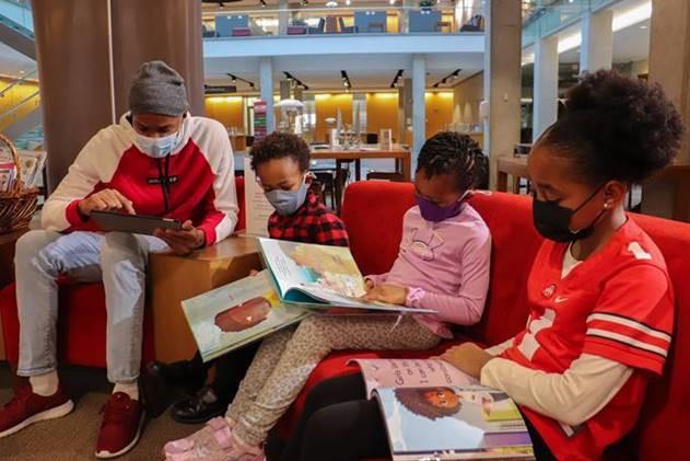 Three children sit in Thompson Library reading children's books