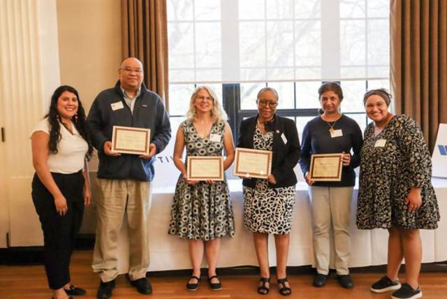 Six people stand in a row, with the middle four holding awards