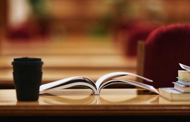 Book laying open on a table with a cup of coffees next to it