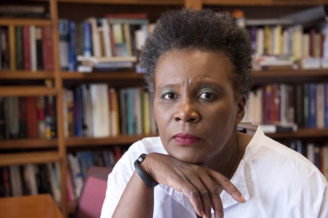 Claudia Rankine, a Black women with short hair, in a light grey blouse, holding her head in her hand