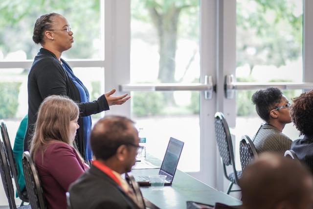 Woman stand behind a table, asking a question during a presentation