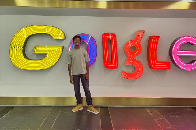 Koury Harmon stands in front of a brightly lit Google sign of many colors