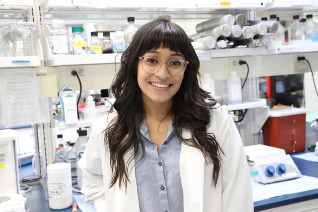 Girl in white lab coat stand in front of shelves of scientific equipment