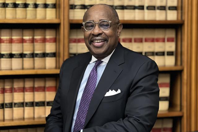 Judge Marbley in a black suit and tie sitting in front of law books, wearing glasses.