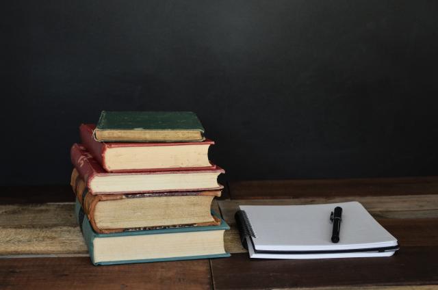 Stack of book sitting next to an open notebook with a pen on it