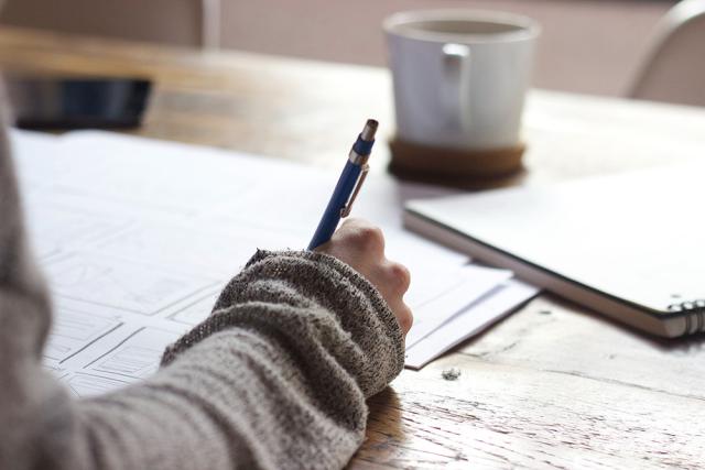 Person writing with a pen on paper with a coffee cup nearby